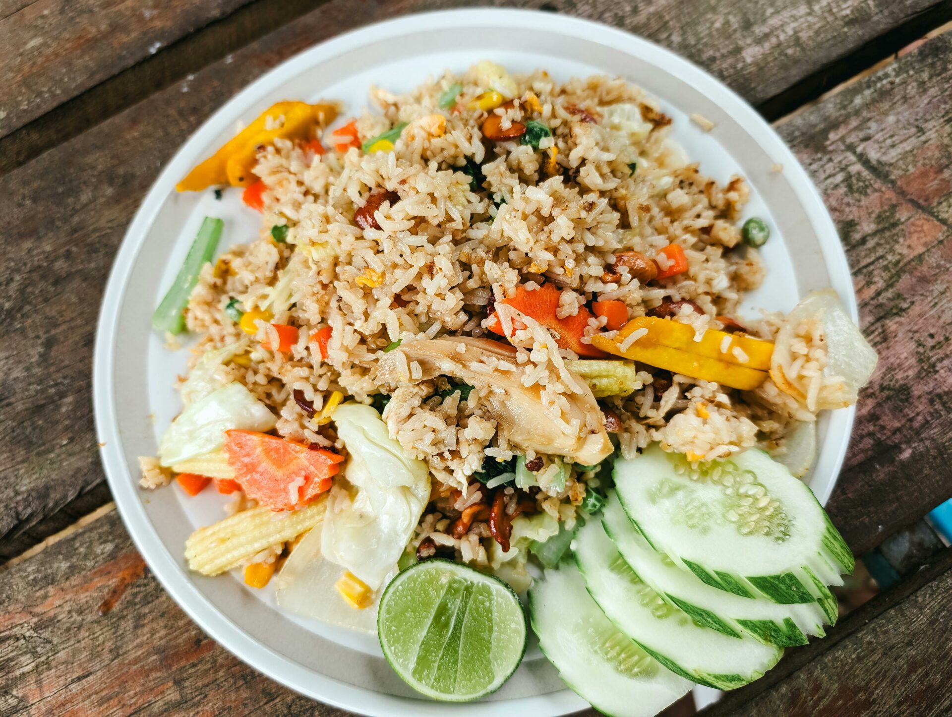 A vibrant plate of vegetable fried rice garnished with fresh cucumber slices and lime, perfect for a healthy meal.