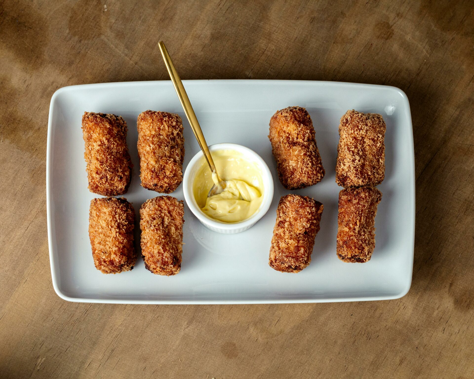 Appetizing crispy croquettes served with dip and garnish on a rustic wooden table.