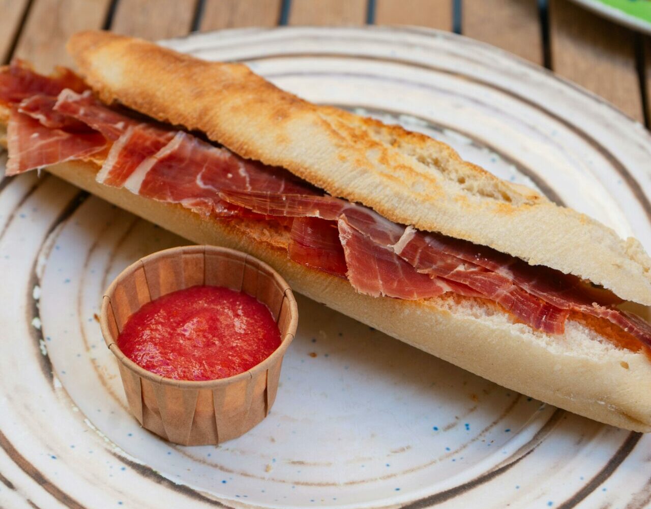 Delicious Spanish bocadillo with jamón and tomato sauce served on a rustic plate outdoors.