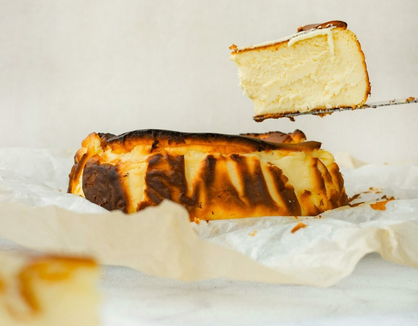 A mouthwatering slice of Basque cheesecake elegantly lifted from the rest, showing its creamy texture.