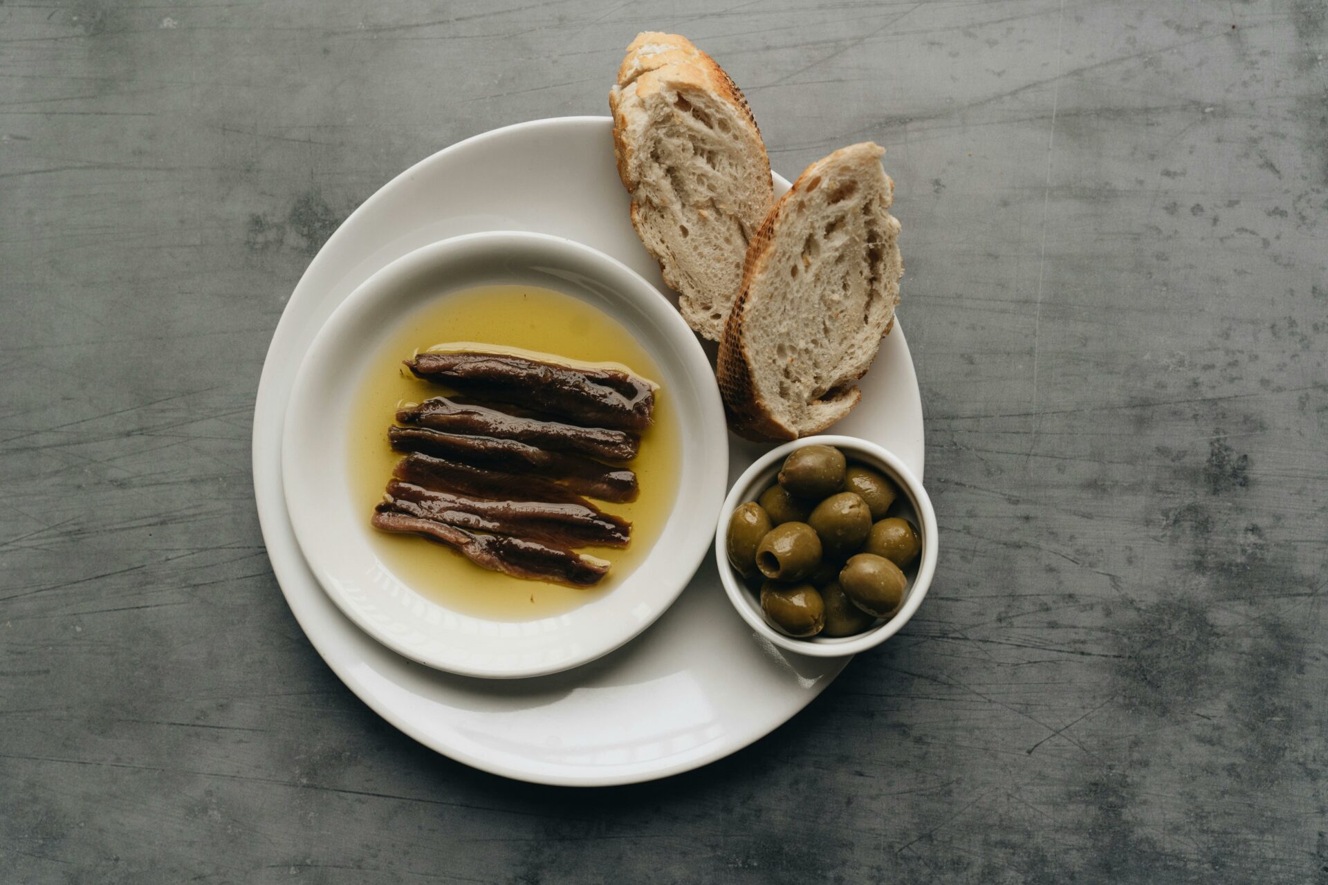 Plate with anchovies, bread, and olives presented in a rustic still life setting.
